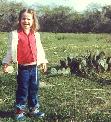 Anna, around 4, standing in their woods, next to a cactus.