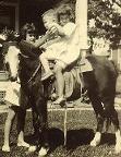 Mom holding her little brother on her pony, with their sister helping.